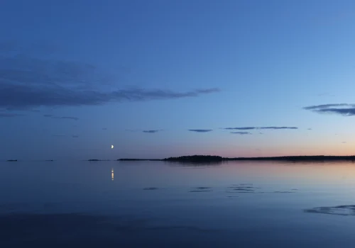Solnedgång över Dragsviksfjärden med månuppgång som speglas i det spegelblanka havet